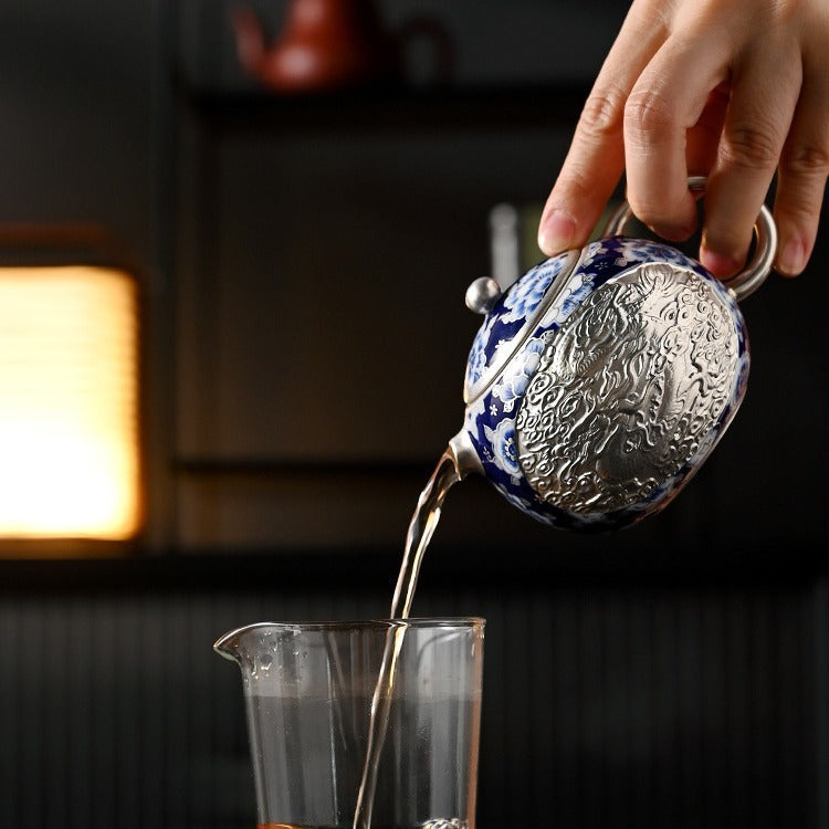 Handcrafted silver "Xishi" style teapot featuring dragon and phoenix relief, blue-and-white accents, and silver gilding; a premium Gongfu tea vessel for home use.