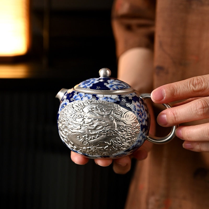 Handcrafted silver "Xishi" style teapot featuring dragon and phoenix relief, blue-and-white accents, and silver gilding; a premium Gongfu tea vessel for home use.